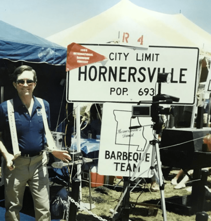 A man stands next to a Hornersville, Missouri city limit sign during a barbecue competition.